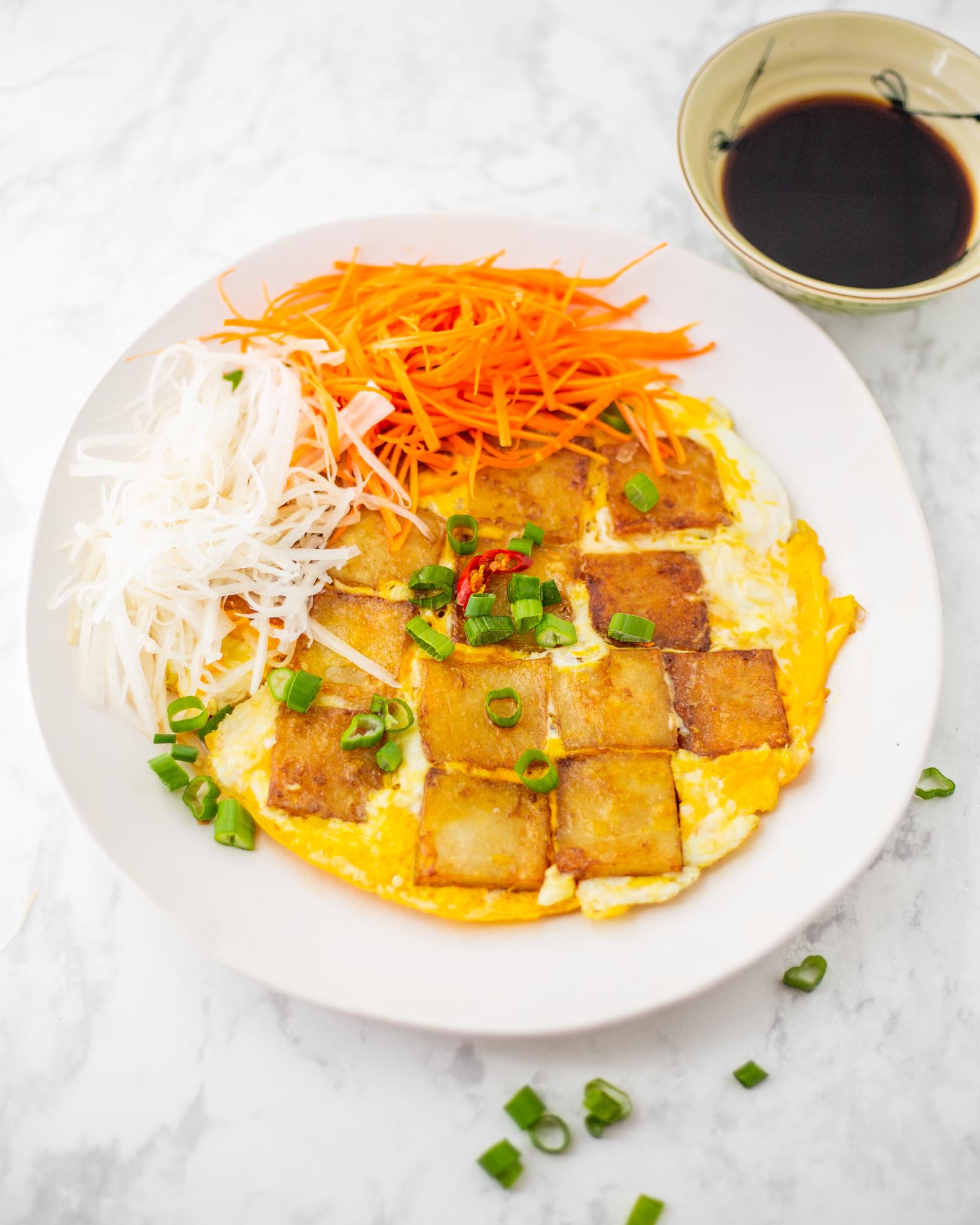 Delicious plate of Bột Chiên, crispy fried rice cakes with eggs and scallions, served with a flavorful dipping sauce