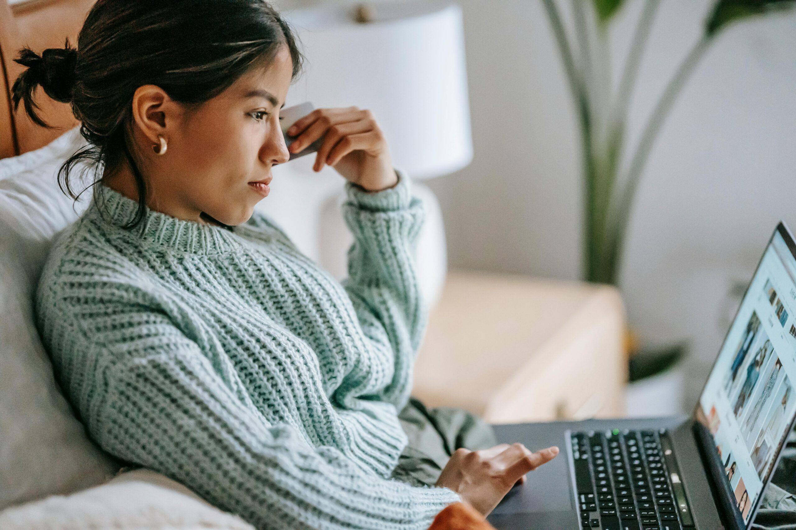 A woman in a cozy green sweater browsing on a laptop while relaxing on a couch at home.