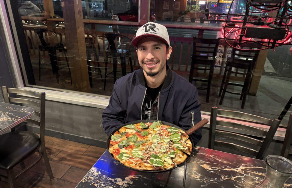 Một người đàn ông đang ngồi bên trong một chiếc bàn với một chiếc bánh pizza trước mặt